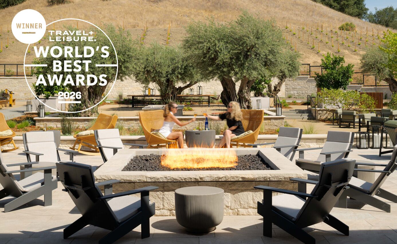 Two guests toast with cocktails beside the fire pit on the olive-tree terrace at Appellation Healdsburg, with the Travel + Leisure World's Best Awards 2026 winner seal