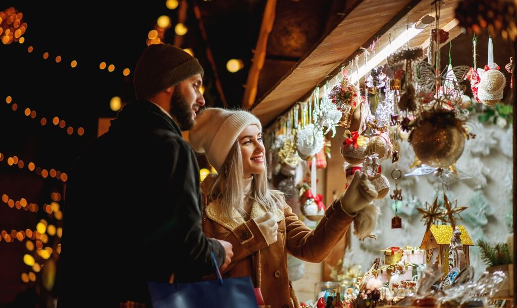 A couple browses handmade ornaments at a lantern-lit holiday market stall