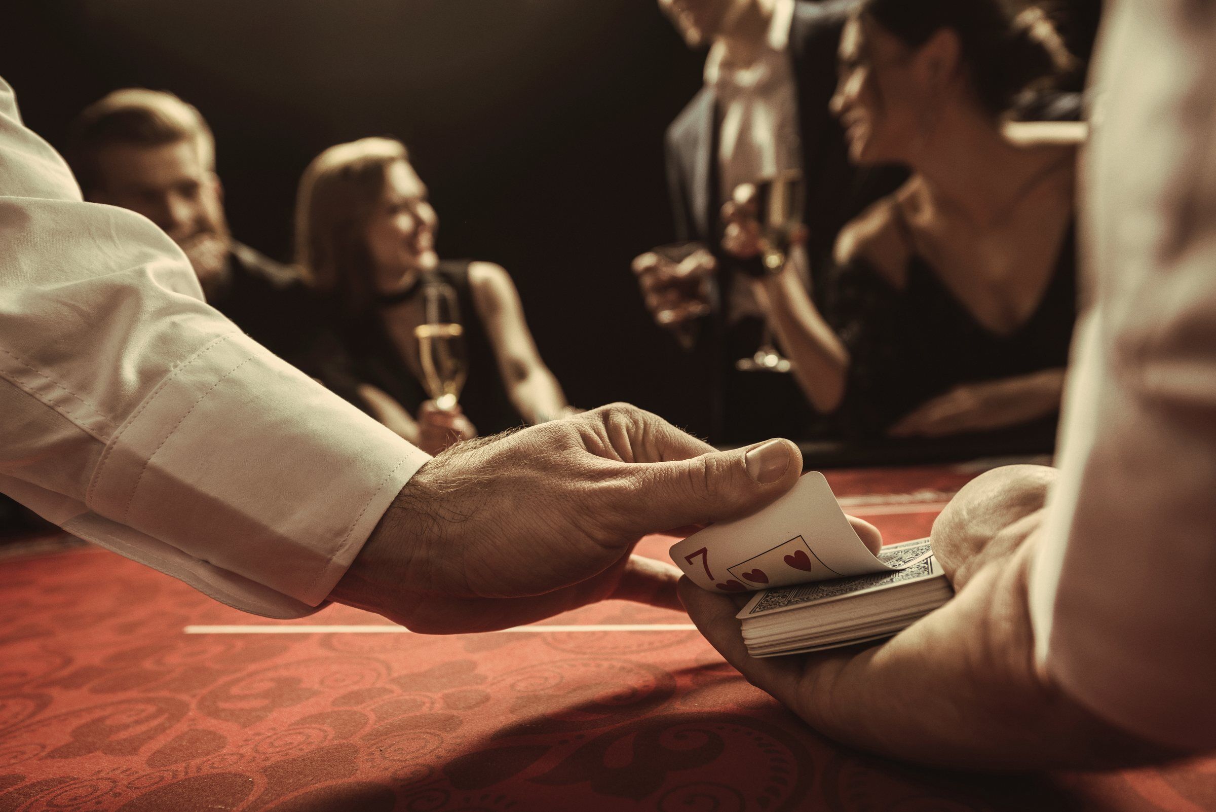 Dealer shuffling cards at a red felt casino table as guests in evening wear raise glasses